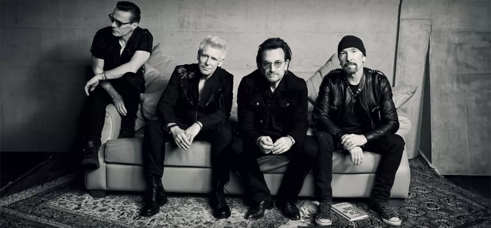 Mitglieder der Band U2 sitzen auf einer Couch. 