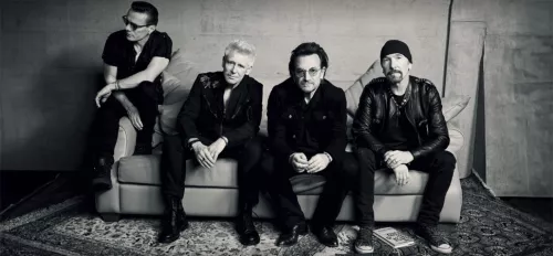 Mitglieder der Band U2 sitzen auf einer Couch. 