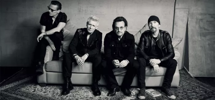 Mitglieder der Band U2 sitzen auf einer Couch. 