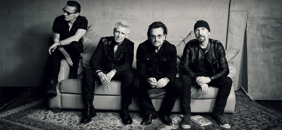 Mitglieder der Band U2 sitzen auf einer Couch. 